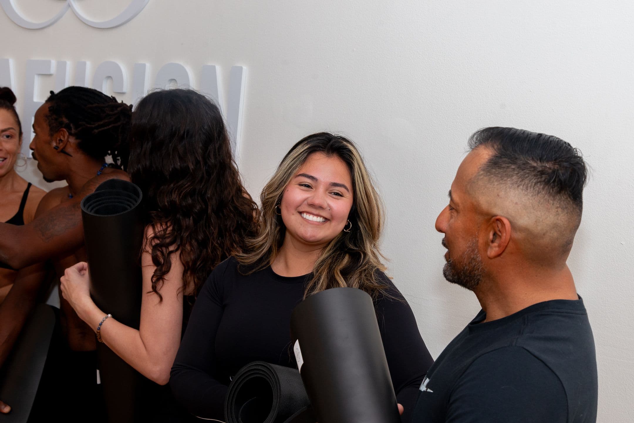 Students smile and talk while holding rolled mats after class.